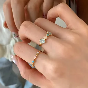 Close-up of gold flower ring with blue enamel and sparkling zircon band on finger