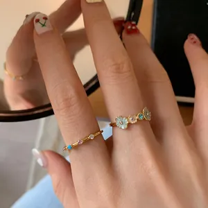 Close-up of golden flower enamel ring and blue zircon band on woman hand