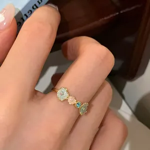 Close-up of golden floral open ring with colorful enamel petals and blue zircon gem