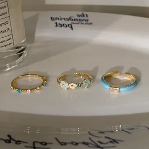 Three dainty adjustable gold rings with blue enamel flowers and sparkling zircon details