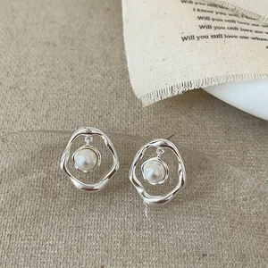 Détail de boucles d'oreilles irrégulières en métal argenté avec perle blanche