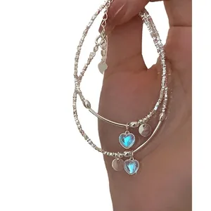 Elegante pulsera de doble cadena de plata con un colgante de corazón azul en la mano