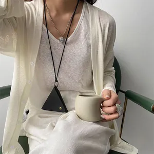 Detailed view of triangular leather pendant and heart necklace on a knit cardigan