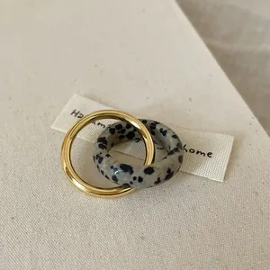 Detail of interlocking gold metal and dalmatian stone rings on soft beige fabric