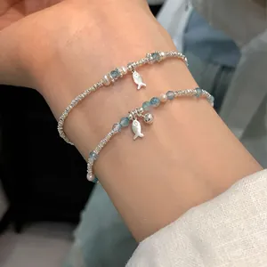 Detail of silver beaded bracelets featuring blue faceted beads and fish charms