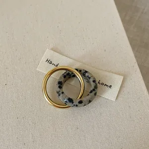 Close-up of interlocking gold metal ring and Dalmatian jasper stone ring on beige fabric
