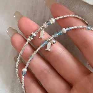 Detail of silver fish bracelet with blue crystal beads and small pearls on wrist