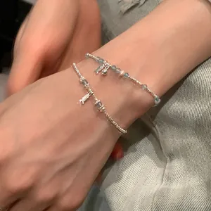 Detail of silver fish charm bracelet with light blue and white beads on a wrist