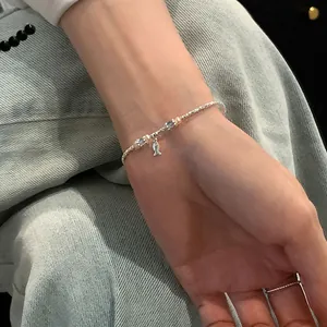 Detail of silver fish charm bracelet with blue crystal beads on wrist against denim
