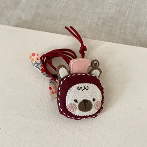 Détail du pendentif ours en tissu fait main avec broderies et motifs floraux sur lin