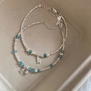 Macro detail of silver bead bracelet set with blue crystals and fish charm on tray