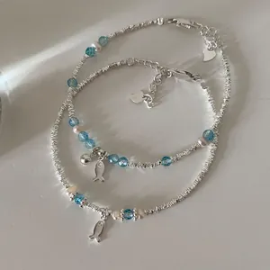 Macro detail of silver fish charms and blue crystal beads on two layered bracelets