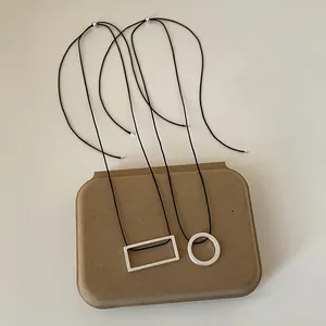 Macro detail of geometric brushed metal pendants with minimalist black cords on a textured base