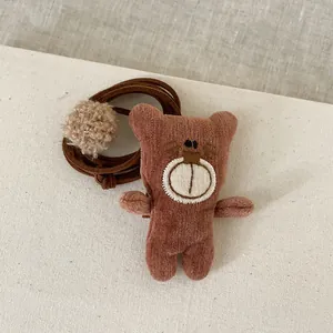 Détail d'un pendentif ours en velours côtelé marron avec broderie et pompon en peluche