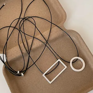 Detailed macro view of brushed geometric pendants on black cord over eco-packaging