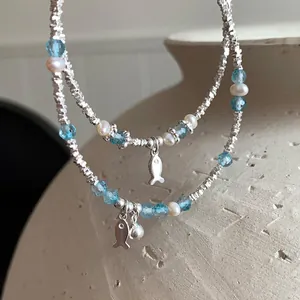 Detail of silver fish charm and blue faceted beads on a double-layered dainty bracelet