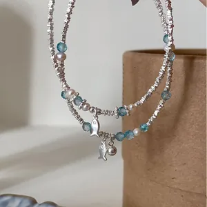 Detailed close-up of a silver fish charm bracelet with blue crystal beads and pearls