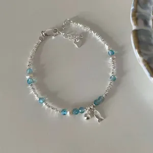Detailed shot of silver fish bracelet with blue crystals and pearls on grey background