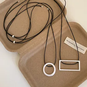 Minimalist geometric brushed metal pendant necklaces with black adjustable cords on a tray