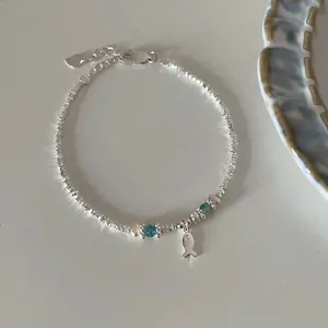 Detail of silver fish charm bracelet with blue beads and pearls on white ceramic