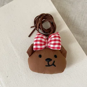 Détail d'un pendentif ours en peluche marron avec nœud à carreaux rouge et broderie
