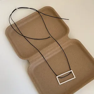 Close-up of a brushed silver rectangular pendant on a black cord necklace in a gift box
