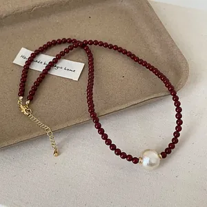 Macro shot of dark red beaded necklace featuring a white pearl and gold metal clasp detail