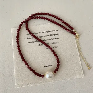 Detail of red beaded necklace with large cotton pearl and golden lobster clasp closure