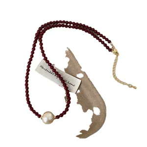 Elegant deep red beaded necklace featuring a central baroque cotton pearl and gold clasp