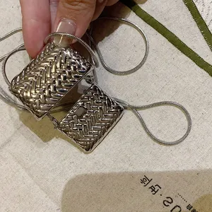 Détail de pendentifs mini sacs tressés argentés sur une fine chaîne serpent