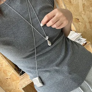 Détail du pendentif de sac tissé argenté et de la breloque goutte sur un t-shirt gris