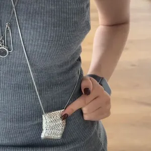 Détail d'un long collier argenté avec un pendentif en métal tissé en forme de sacoche