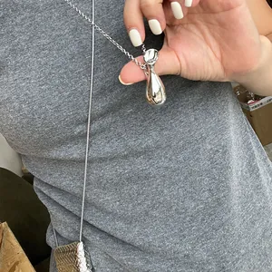 Gros plan du pendentif goutte d'argent poli avec chaîne fine sur fond de tissu gris