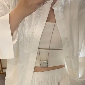 Gros plan d'un collier pendentif carré tressé argenté sur une blouse en dentelle