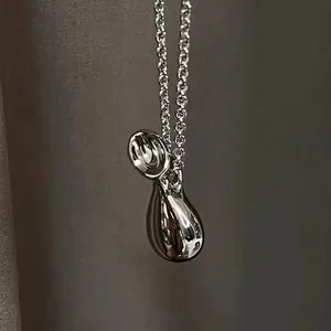 Détail macro du pendentif goutte en métal argenté fluide avec une finition miroir