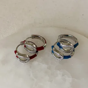 Macro detail of U-shaped enamel hoop earrings with inlaid zircons on marble surface