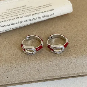 Detail view of horseshoe-shaped silver earrings with red enamel and pavé zircon stones