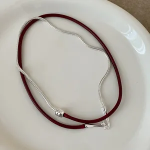 Detail van rood koord en zilveren slangenketting met een minimalistische sluiting