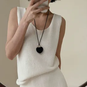 Detalle de un collar con colgante de corazón negro combinado con un atuendo de punto