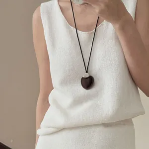Detalle de un collar con colgante de corazón minimalista de cuero sobre un chaleco de punto