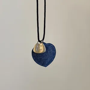 Detalle de colgante de corazón de mezclilla azul con grabado en cuerda tejida negra