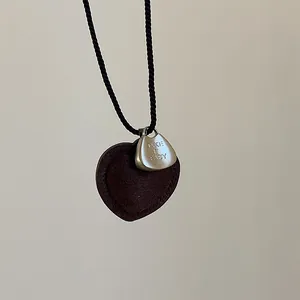Detalle del collar de corazón con grabado TAKE IT EASY y base de gamuza marrón suave