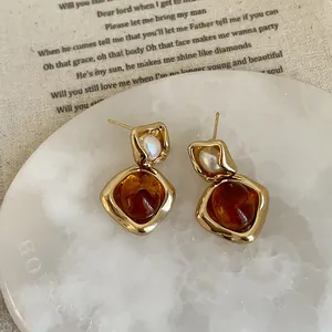 Irregular amber resin and pearl earrings in gold frame on marble texture background