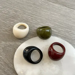Detailed shot of thick resin dome rings in cream, olive, black, and burgundy on a stone tray