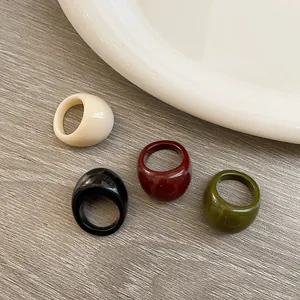 Close-up of four thick resin rings in beige black burgundy and olive green