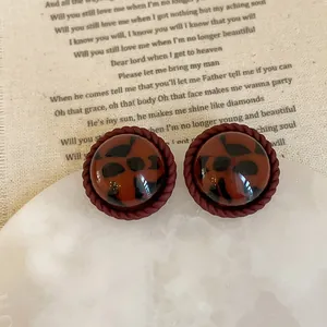Macro detail of vintage leopard print resin earrings with dark red twisted rope borders