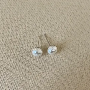 Detail of round pearl stud earrings with metallic sheen on beige textured background