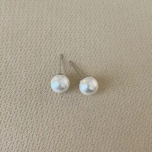 Detailed view of elegant round white pearl earrings with silver posts on textured base