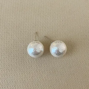 Detail of irregular hammer-textured cream pearl earrings with silver posts for women