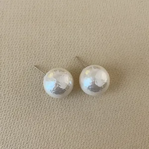 Close-up of pearl white stud earrings with hammered texture on beige fabric
